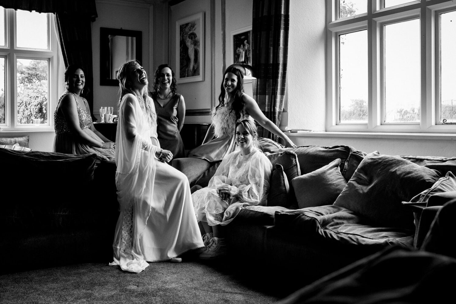 bride and bridesmaids laughing whilst sitting on a sofa at ash barton estate wedding by devon wedding photographer mike wells